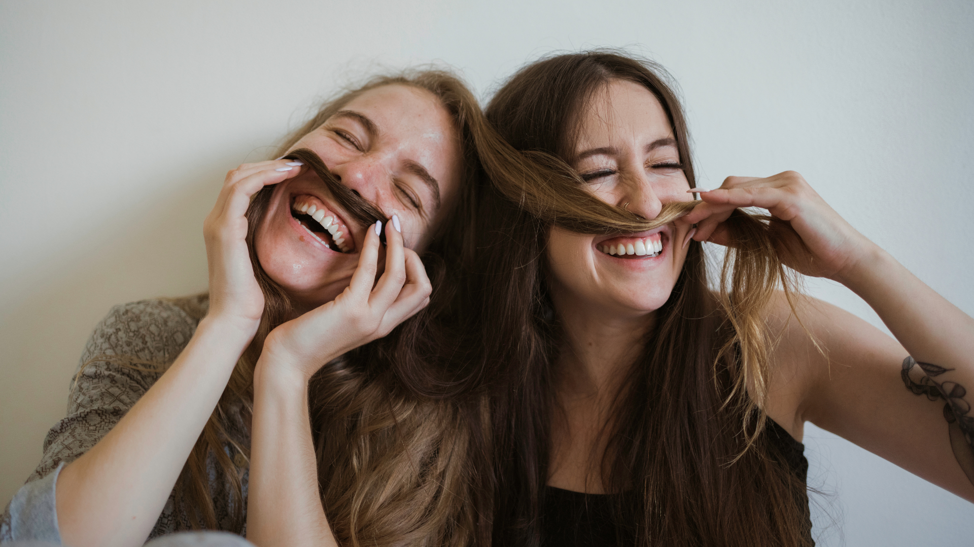 two women laughing while joking with their hair pretending their hair is their moustache.