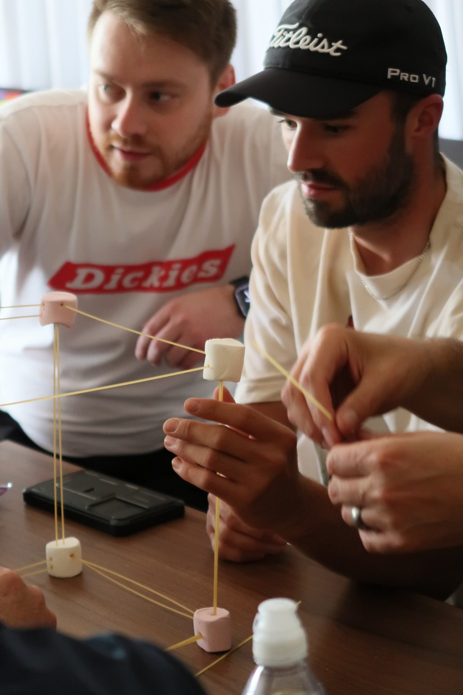 2 men building a tower out of marshmallows and spaghetti